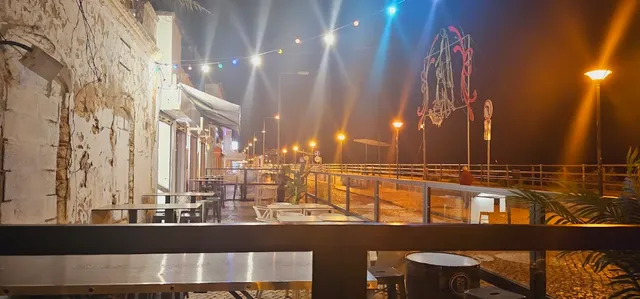 An evening terrace beside a promenade lit by strings of bulbs and street lamps