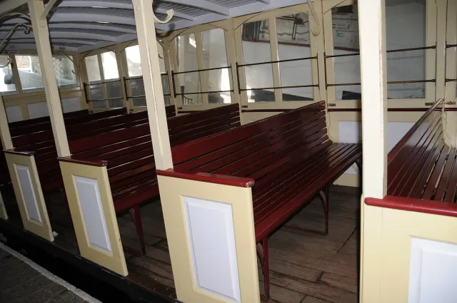 The interior of a heritage carriage with red wooden benches and pale partitions