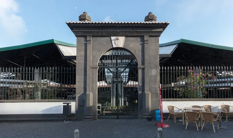 An arched basalt stone gateway into a market, with green canopies and stalls behind