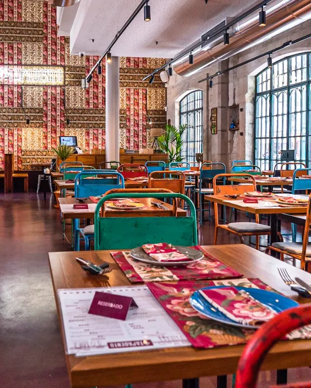 A colourful room with printed wallpaper, green and blue metal chairs and a set table