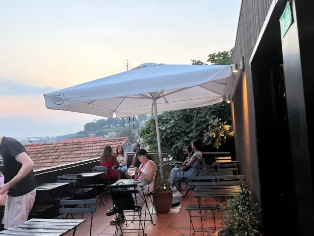 A terrace at dusk with a white parasol, diners and a distant rooftop view
