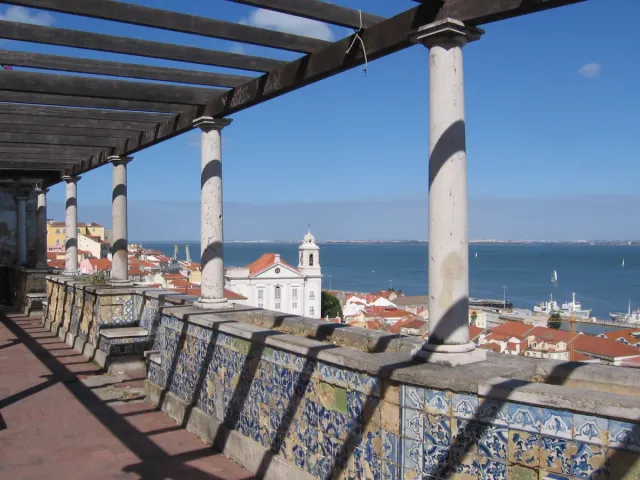 A pergola with columns and painted tiles above tiled roofs and a river