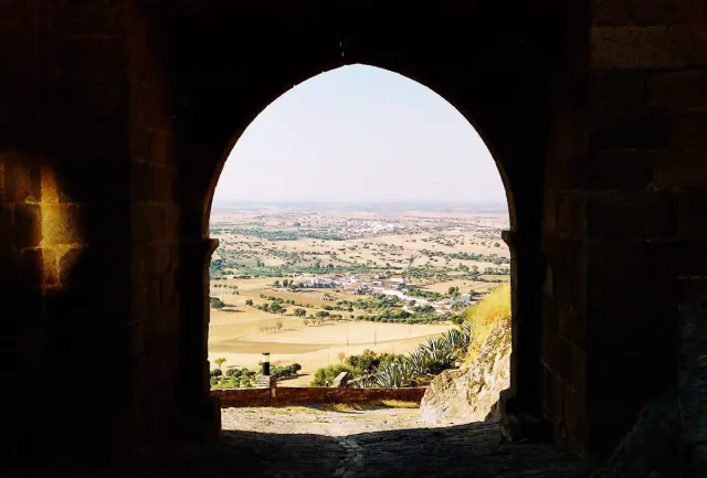A dark arched stone gate framing an open plain to the horizon