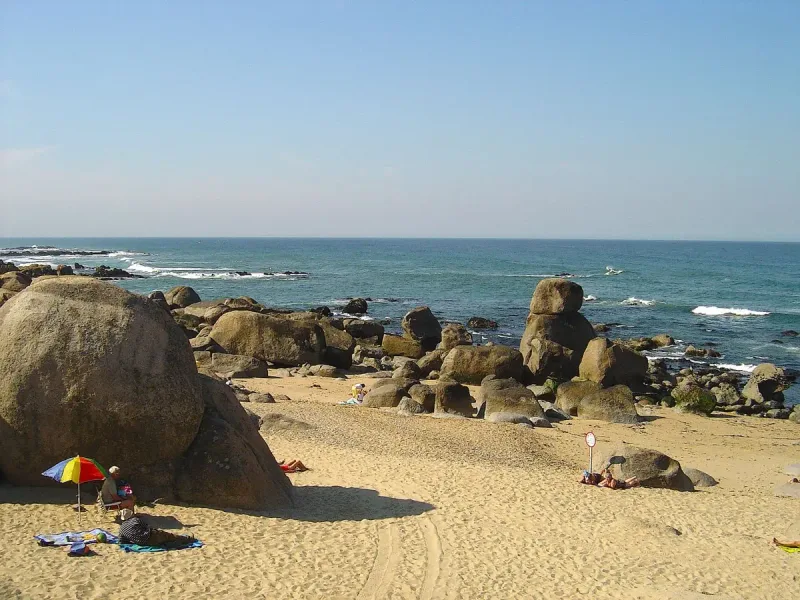 Huge granite boulders scattered across golden sand facing a blue sea