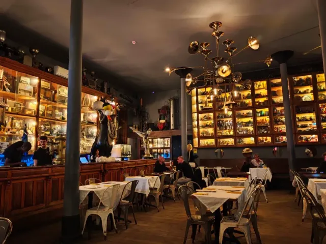 A hall with wooden cabinets full of objects, a brass chandelier and set tables