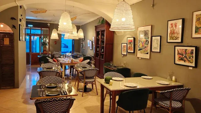A room with woven hanging lamps, framed pictures on a green wall and cane chairs