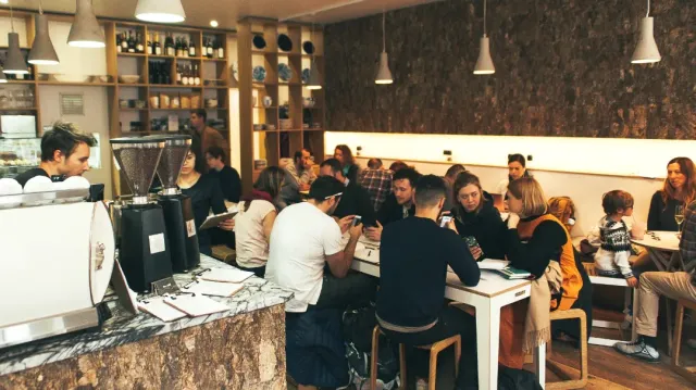 A space crowded with people, a cork wall, white lamps and a marble counter with grinders