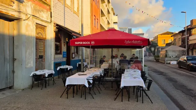 Street tables with white cloths and a red parasol facing a tiled building in sunset light