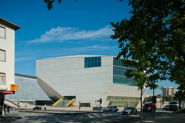 An angular white concrete building with huge glass windows beside a street
