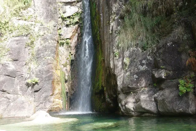 A narrow waterfall dropping between rock walls into a turquoise pool