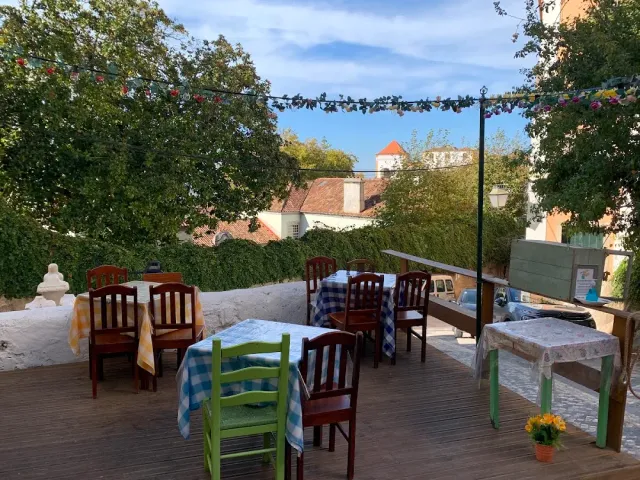 A wooden deck with checkered tablecloths under a string of bunting, facing red roofs and trees