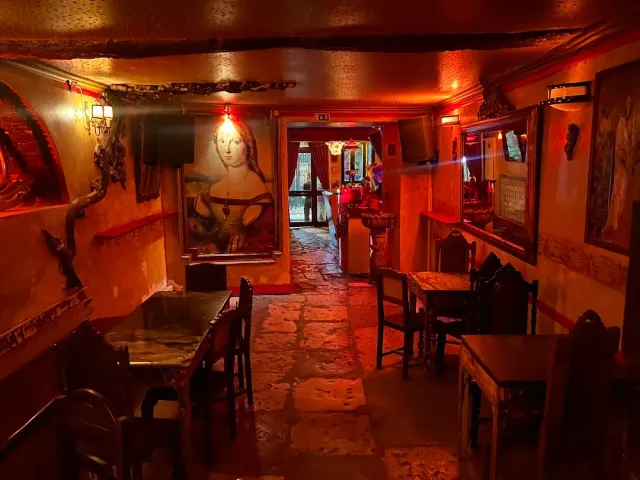 A vaulted space in red light with a stone floor, a portrait painting and wooden chairs