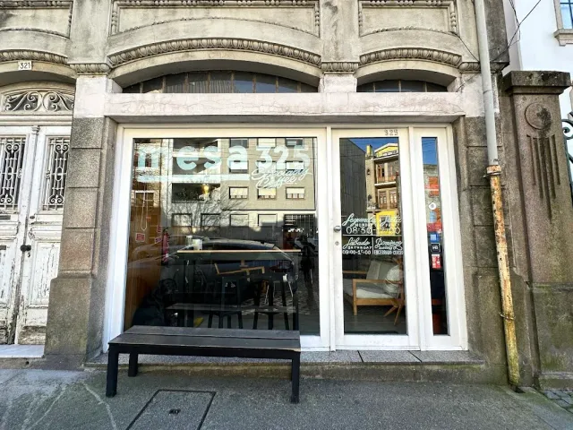 A large shop window in a stone building, a wooden bench outside and tables seen inside