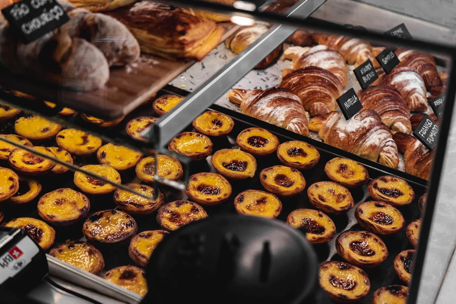 Glass display case of Portuguese pastries beside a marble counter in a traditional pastelaria