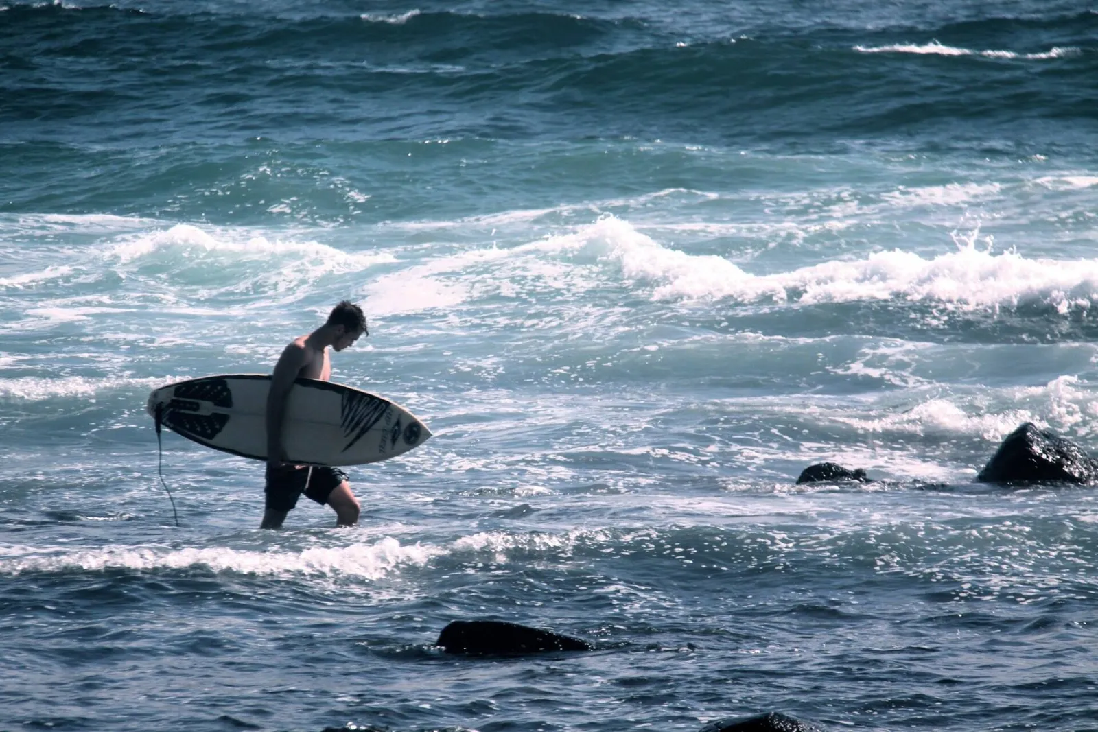 A surfer walking into the water with a surfboard on a sunny Portuguese beach